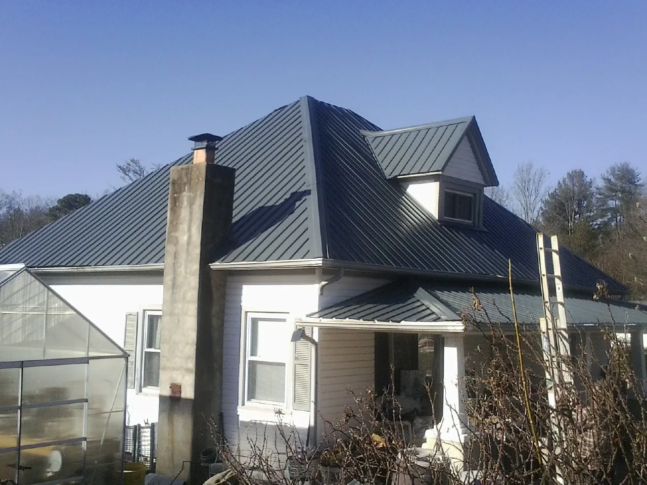 Dark blue standing seam metal roof on a white farmhouse with dormer — Slate & Tile Roof Repair by Roofing Brothers in Hanley Falls