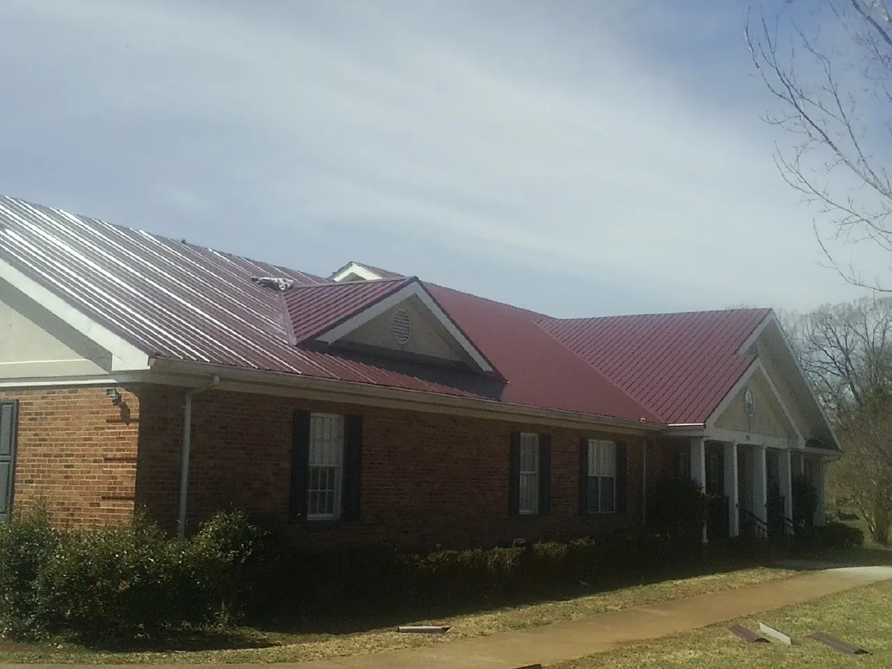 Red metal roof with gabled entries on a long brick building, from a Hail Damage Roof Repair job in Hanley Falls