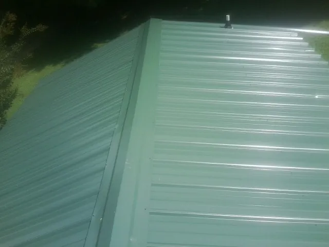 New green metal panels meeting at the ridge of a roof — Flat Roof Repair work by our crew in Hanley Falls
