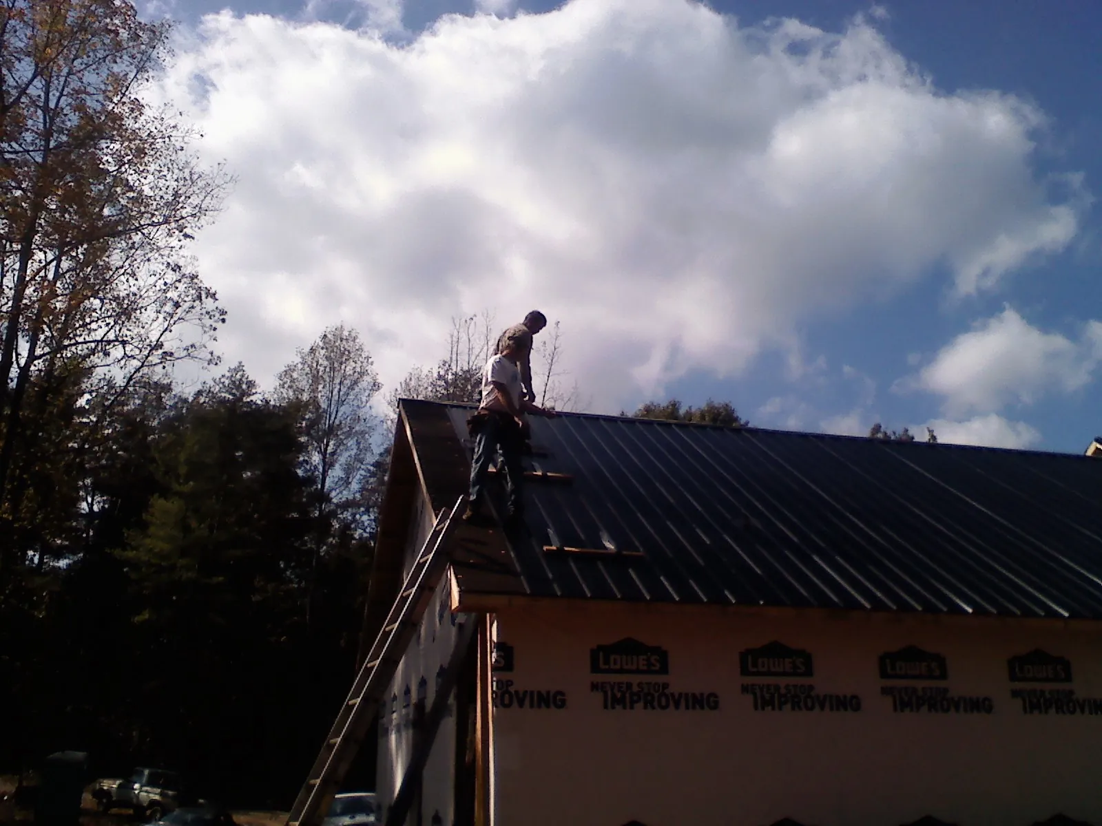 Roofer fastening dark metal panels high against a cloudy sky, from a Roof Inspection job in Hanley Falls