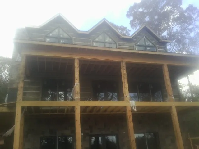Dormers and porch framing on a large log home under construction — Roof Coating work by our crew in Hanley Falls