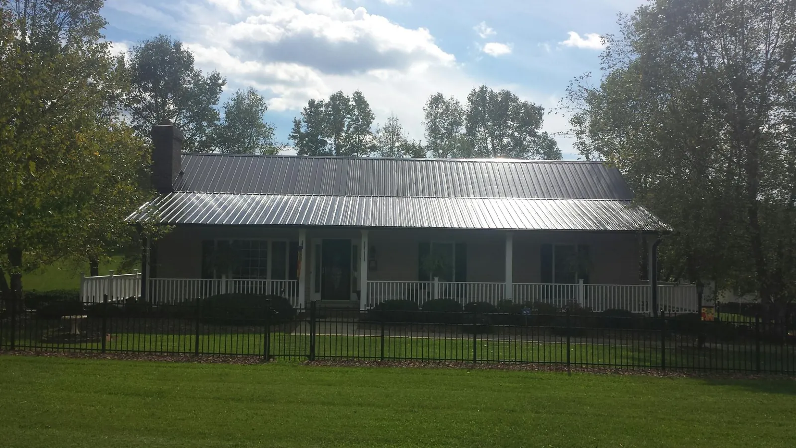Gray metal roof on a brick ranch with a full width front porch — Gutter Guard Installation work by our crew in Hanley Falls
