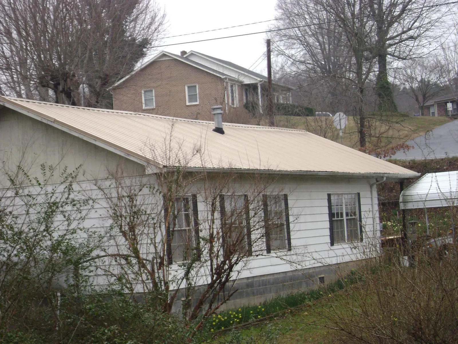 Tan metal roof on a white sided house set into a hillside — Commercial Roofing by Roofing Brothers in Hanley Falls