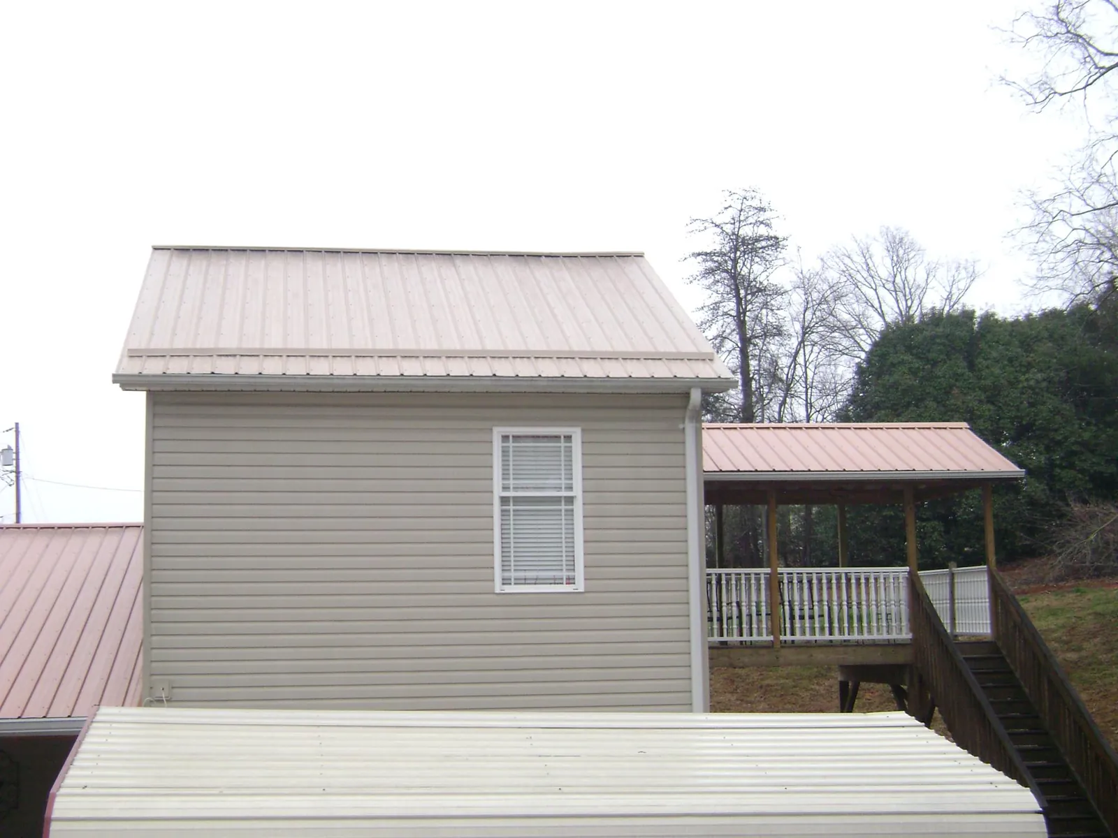 Tan metal roofs on a two story addition and attached porch, from a Roof Replacement job in Hanley Falls